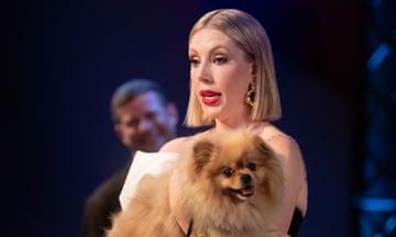 Katherine Ryan holding a pomeranian dog in her arms in Silence is Golden, with Dermot O'Leary blurred out in the background