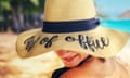 woman on beach wearing straw sunhat with words 'out of office' on it