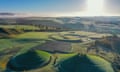 Crawick Multiverse in Dumfries and Galloway - an aerial view of rolling hills, with large mounds in the foreground, with stone circles on top of them