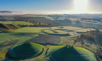 Crawick Multiverse in Dumfries and Galloway - an aerial view of rolling hills, with large mounds in the foreground, with stone circles on top of them