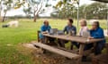 Four people sitting at an outdoor table with open laptops in front of them with pasture and a cow in the background