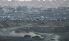 Israeli tanks driving in the deserted outskirts of Gaza, with destroyed building in the background.