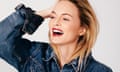 Headshot of Heather Graham laughing, in denim jacket with one hand holding back her hair
