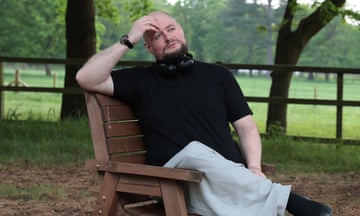 Richard Wordsworth sits on a park bench, wearing a black T-shirt and grey trousers