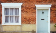 The front of a house with a wooden front door painted pale blue-grey and a sash window with net curtains