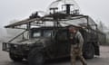 Ukrainian soldier walks past a Humvee covered in metal framing, wire netting and other drone defences