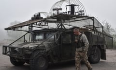 Ukrainian soldier walks past a Humvee covered in metal framing, wire netting and other drone defences
