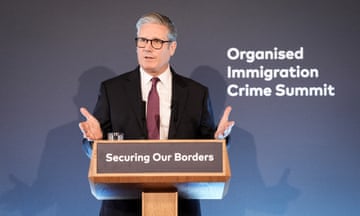 Keir Starmer standing at a lecturn that has a slogan on the front: Securing Our Borders. Behind him to his left is another slogan: Organised Immigration Crime Summit.