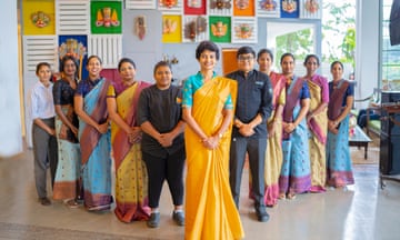 A group of women stand in a staggered line in a hotel foyer, most wearing saris