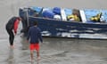 lifeguards stand in shallow water at beach and look at a capsized boat