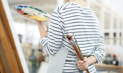 Back view portrait of a female artist holding brushes standing next to easel in art studio, copy space