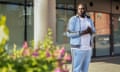 Ade Adedeji: he stands in front of a building at De Montfort University in Leicester with tall glass windows, with a bush and pink flowers in the foreground; he wears a white T-shirt and pale blue tracksuit.