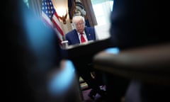 man wearing navy suit and red tie sits at table and looks down